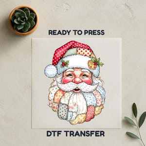 Op de afbeelding: Een kleurrijk ontwerp van de Kerstman met een patchwork hoed en baard, klaar om te persen. De afbeelding bevat de tekst "READY TO PRESS" en "DTF TRANSFER". De Kerstman heeft een roze gezicht en een witte snor.
