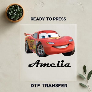 Op de afbeelding: Een rode Lightning McQueen DTF-transfer met de naam "Amelia" in zwart script. De afbeelding bevat ook de tekst "READY TO PRESS" en "DTF TRANSFER".