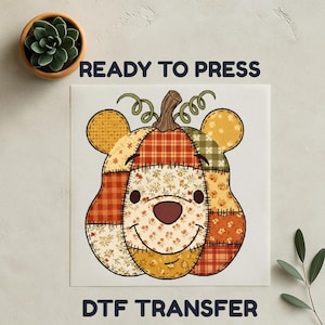 Op de afbeelding: Een DTF-transfer met een patchwork ontwerp van een lachende beer-vormige pompoen. Het ontwerp gebruikt oranje, gele en groene patronen. De tekst "READY TO PRESS" en "DTF TRANSFER" worden weergegeven.