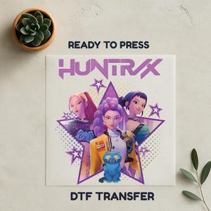 May include: A DTF transfer featuring three stylized female figures within a purple star design. The transfer includes the text "HUNTRAX" and "READY TO PRESS" and a blue cat figurine.