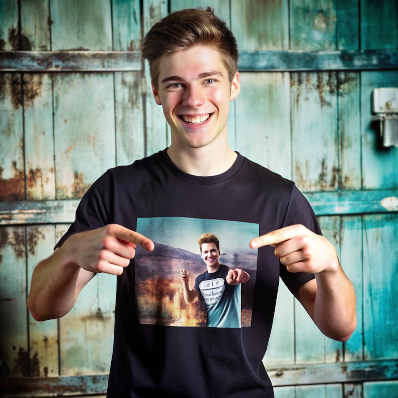 May include: A black crew neck t-shirt featuring a photographic print of a person pointing. The person in the image is also wearing a t-shirt with a graphic. The background is a rustic, teal-colored wooden door.