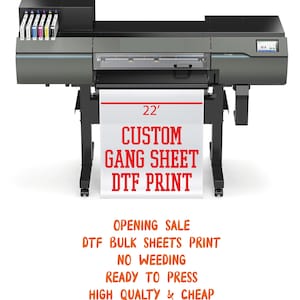 May include: A large format printer with a white banner displaying "CUSTOM GANG SHEET DTF PRINT". The banner is 22 feet wide. The printer is black and gray, with ink cartridges visible on top.