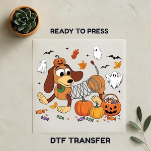 Op de afbeelding: Een DTF-transfer met een cartoonhond met een veerkrachtig lichaam, met een pompoen op zijn hoofd, omringd door geesten, vleermuizen en pompoenen. De woorden "READY TO PRESS" en "DTF TRANSFER" zijn afgedrukt.