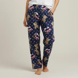 Könnte beinhalten: Eine Frau trägt ein weißes Kurzarm-T-Shirt und eine marineblaue Schlafhose. Die Schlafhose hat ein Muster aus braunen Teddybären, weißen Punkten und roten und rosa Geschenkboxen. Sie steht da und hat eine Hand in der Tasche.