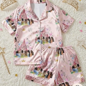 Turn bedtime into a royal slumber party with this super cozy custom pajamas set featuring all your favorite Disney Princesses (Snow White, Cinderella, Aurora, Ariel, Belle, Jasmine, Pocahontas, Mulan, Tiana, Rapunzel, Merida, Moana) gathered together in front of the sparkling castle, chatting, laughing, with fireworks, hearts, stars & magical sparkles on a soft pastel pink background