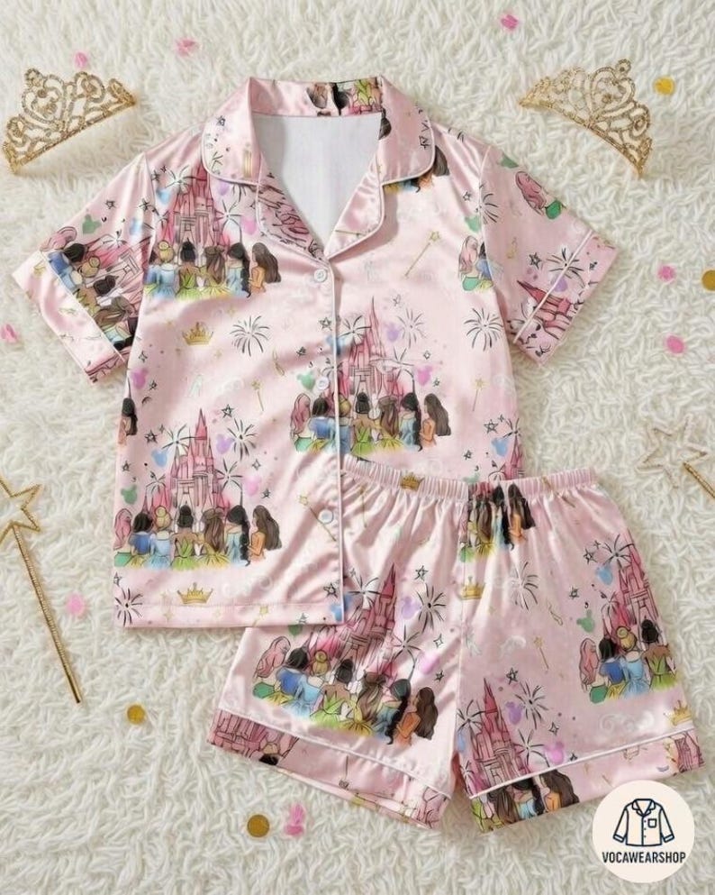 Turn bedtime into a royal slumber party with this super cozy custom pajamas set featuring all your favorite Disney Princesses (Snow White, Cinderella, Aurora, Ariel, Belle, Jasmine, Pocahontas, Mulan, Tiana, Rapunzel, Merida, Moana) gathered together in front of the sparkling castle, chatting, laughing, with fireworks, hearts, stars & magical sparkles on a soft pastel pink background