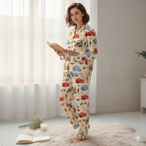 Peut inclure: Ensemble de pyjama beige avec un motif de voitures de dessins anim&eacute;s rouges, bleues et marron. Le haut &agrave; manches longues a une fermeture boutonn&eacute;e et un col crant&eacute;. Le pantalon assorti a une taille &eacute;lastique. La personne tient un livre.