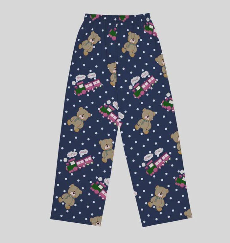 May include: Navy blue pajama pants with a repeating pattern of teddy bears, toy trains, and white polka dots. The bears are tan with green scarves, and the trains are pink and green. The pants have a relaxed fit.