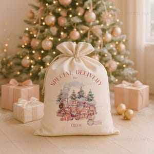 Puede incluir: Una bolsa de regalo crema con cordón con el texto "SPECIAL DELIVERY" y una ilustración de acuarela de un tren, Papá Noel y un muñeco de nieve. La bolsa está atada con un cordón de color natural y tiene el nombre "CHLOE" impreso.