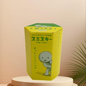 May include: A yellow hexagonal box with the text "SMISKI GLOW IN THE DARK Series 1" in English and Japanese. The box features a cartoon character and Japanese text. The box is on a white pedestal.