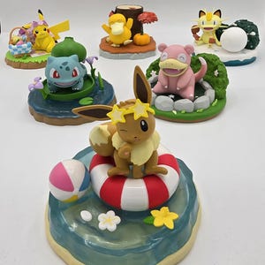 May include: A collection of colorful Pokémon figurines. The figurines include Pikachu, Bulbasaur, Psyduck, Meowth, Slowpoke, and Eevee. Each figure is set on a themed base, with details like a beach ball, flowers, and a picnic basket.