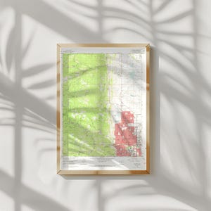 Könnte beinhalten: Eine gerahmte topografische Karte mit einem hellen Holzrahmen. Die Karte zeigt grüne, weiße und rote Bereiche, die wahrscheinlich Gelände und Stadtentwicklung darstellen. Die Karte ist detailliert mit Höhenlinien und Text.