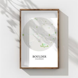Könnte beinhalten: Ein gerahmter Druck mit einer Karte von Boulder, Colorado, in einem kreisförmigen Design. Die Karte ist in Grau- und Grüntönen gehalten, mit dem Namen der Stadt und des Bundesstaates darunter. Der Rahmen ist aus dunklem Holz.