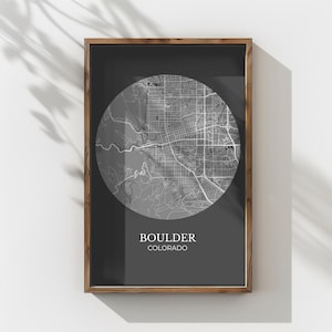 Könnte beinhalten: Gerahmter Graustufen-Kartendruck von Boulder, Colorado. Die Karte ist ein detailliertes kreisförmiges Design vor einem dunkelgrauen Hintergrund. Der Rahmen hat eine warme braune Farbe, und der Text "BOULDER COLORADO" befindet sich unten.