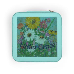 May include: A square, pale blue jewellery case with a floral design. The artwork features a variety of colourful flowers, including yellow sunflowers, white daisies, and pink blossoms, with the text "Lydia Grace" in cursive.