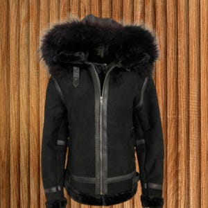 Puede incluir: Chaqueta negra de borrego con capucha forrada de piel. La chaqueta presenta una cremallera frontal, ribetes de cuero y una cintura con hebilla. Las mangas tienen ribetes de cuero y puños de piel.