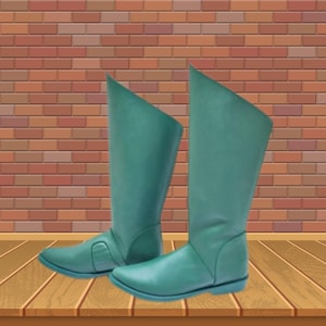 Puede incluir: Un par de botas altas de color verde azulado. Las botas tienen una textura suave y un ligero brillo, con un borde superior doblado. Las botas están colocadas contra una pared de ladrillo y un suelo de madera.