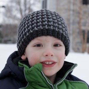 May include: A young person wearing a gray and black knit hat with a green and blue winter jacket.