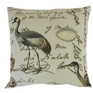 May include: Beige throw pillow with a brown and gray crane and bird design. The pillow has a cream background with brown script writing that says "This morning sorgt Gap on the Netut opposite. Mdo of M Nee fi Balch Lie $5".