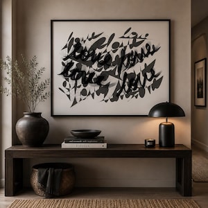 May include: A rectangular wall art piece featuring black abstract shapes and the word love repeated in black script. The artwork is framed in black and displayed above a dark wooden bench holding a black vase, books, and a black dome-shaped lamp.