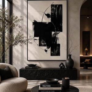 May include: A large framed abstract painting featuring bold black geometric shapes and thin lines on a cream background, displayed above a black textured console table with a black vase, a bowl, and a decorative knot object.