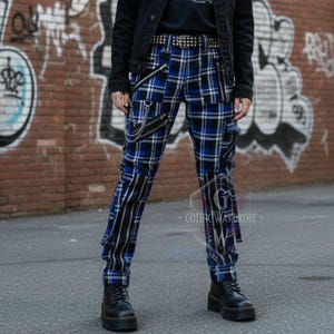 May include: Blue and black plaid pants with silver chain detailing and black boots. The pants have a blue and white plaid pattern with vertical black stripes on the sides. A black denim jacket and studded belt complete the look.