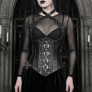 May include: Black leather corset with silver-colored buckles and rivets. The corset has a halter-style neckline and is worn over a sheer black top. The overall style is gothic and edgy.
