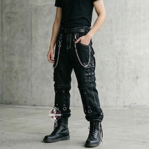 May include: Black cargo pants with multiple pockets, silver chain accents, and metal ring details. The pants have a straight leg fit and are paired with black boots. The pants are made of a dark denim material.