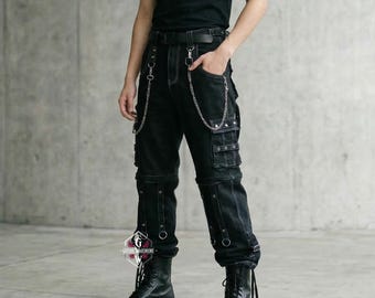 May include: Black cargo pants with multiple pockets, silver chain accents, and metal ring details. The pants have a straight leg fit and are paired with black boots. The pants are made of a dark denim material.