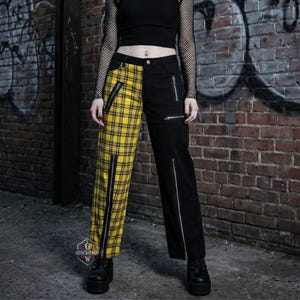 May include: Black and yellow plaid split-leg pants with silver zippers. One leg is yellow plaid, the other is solid black. The pants have multiple silver zippers and are worn with black platform boots.