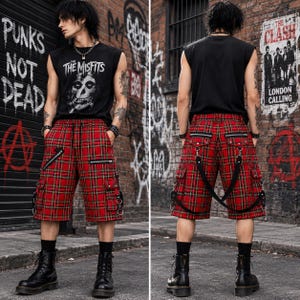 May include: Red plaid shorts featuring multiple cargo pockets, silver-tone metal zippers, and attached black straps with metal D-rings. The shorts have a drawstring waist and are paired with a black sleeveless shirt with a white Misfits graphic.