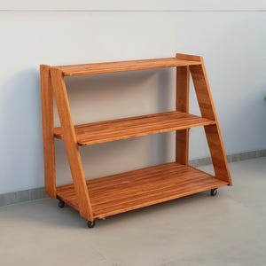 May include: A three-tiered wooden plant stand with a warm, reddish-brown finish. The stand has an A-frame design with three shelves and small wheels for mobility. The shelves are made of horizontal wooden slats.