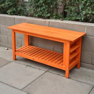 Op de afbeelding: Oranjehouten bank met een lattenbodem en zijplanken. De bank heeft een rechthoekige bovenkant. De bank is gemaakt van hout en geschikt voor buitengebruik. Afmetingen in centimeters.