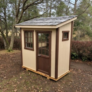 May include: A small, wooden shed with a beige exterior and brown trim. It has a sloped roof, a door with multiple panes of glass, and two windows. The shed is set on a wooden base and is surrounded by trees.