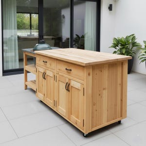 Può includere: Un'isola cucina esterna in legno chiaro con grill integrato. L'isola ha un piano di lavoro in legno, cassetti e ante con maniglie nere. Poggia su ruote e ha un ripiano laterale. Un grill verde è sul piano di lavoro.