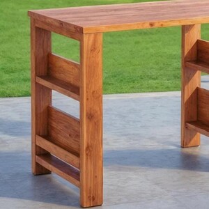 Op de afbeelding: Een houten bartafel met een natuurlijke afwerking. De tafel heeft een rechthoekig blad en een onderste plank aan elke kant. De tafel is gemaakt van massief hout en heeft een eenvoudig, modern ontwerp. De tafel is ongeveer 102 cm lang.