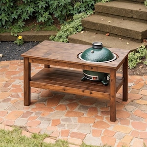 Può includere: Un tavolo da cucina all'aperto in legno marrone scuro con una griglia in ceramica verde incorporata. Il tavolo ha un ripiano inferiore per riporre gli oggetti ed è posizionato su un patio in mattoni. La griglia è uno stile popolare per cucinare all'aperto.