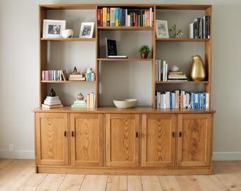 Puede incluir: Una gran librería de madera clara con múltiples estantes y armarios. La librería está llena de libros, objetos decorativos y fotos enmarcadas. La madera tiene un acabado natural y el diseño es clásico y funcional.