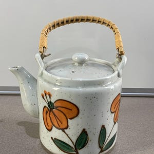 May include: A set of three ceramic mugs with a speckled, cream-colored glaze. Each mug features a different hand-painted design: a blue and green leaf, a yellow flower, and a red berry. The mugs have a simple, modern design.