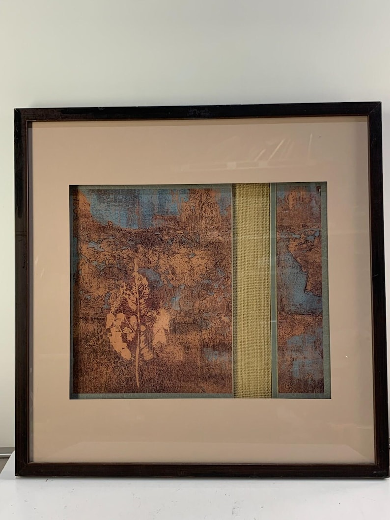 Puede incluir: Impresi&oacute;n art&iacute;stica abstracta enmarcada con un marco de madera marr&oacute;n. La obra de arte presenta un dise&ntilde;o texturizado con colores marr&oacute;n, azul y beige. Una tira vertical de tela verde claro divide la obra. La impresi&oacute;n est&aacute; sobre un passe-partout beige.
