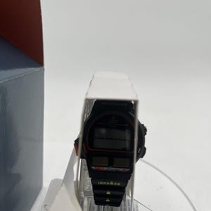 May include: Black Ironman Triathlon watch with a digital display. The watch has red accents and the Ironman logo. The watch is in its original packaging, with the words "Ironman" and "Indiglo" visible.