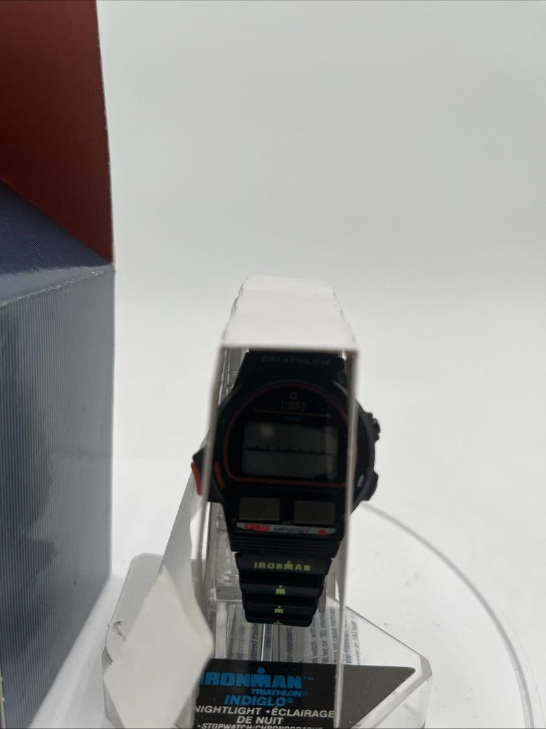 May include: Black Ironman Triathlon watch with a digital display. The watch has red accents and the Ironman logo. The watch is in its original packaging, with the words "Ironman" and "Indiglo" visible.