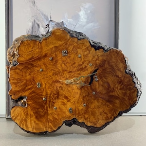 May include: A distinctive wall clock made from a tree trunk cross-section. The clock face displays natural wood grain in brown and gold tones, with brass-coloured hands and hour markers. The clock measures approximately 50 cm in diameter.
