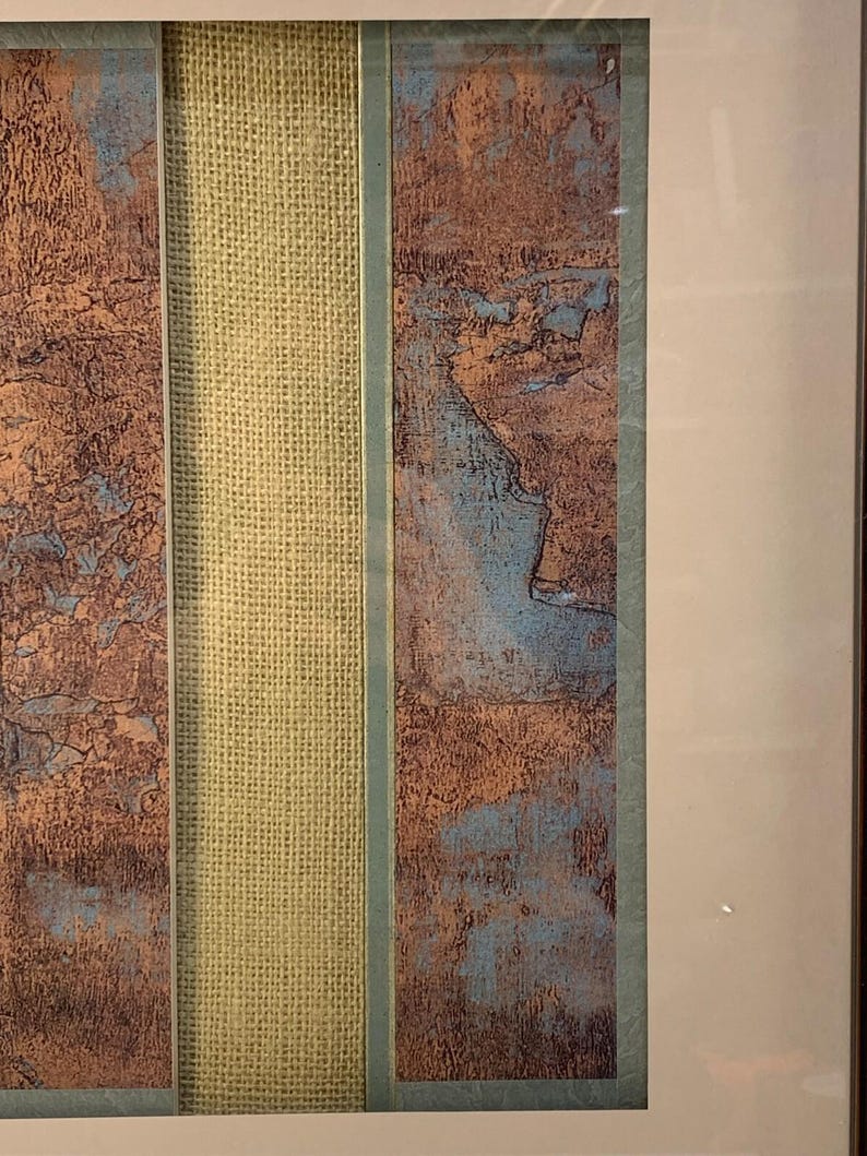 Puede incluir: Obra de arte abstracta enmarcada con paneles texturizados en tonos marr&oacute;n y azul, separados por una secci&oacute;n central de arpillera beige. La obra est&aacute; encerrada en un marco blanco, creando una est&eacute;tica moderna.