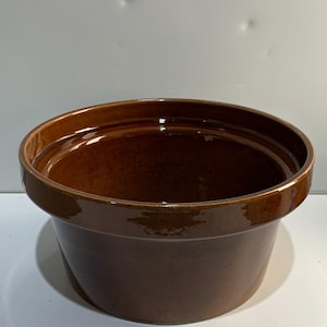 May include: A brown ceramic bowl with a glossy finish. The bowl has a wide, rounded rim and a slightly tapered body. The interior is a darker shade of brown. The bowl is likely used for serving or food preparation.
