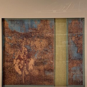 Puede incluir: Obra de arte abstracta enmarcada con una apariencia texturizada. La obra presenta una combinaci&oacute;n de tonos marrones, azules y beige, con una tira vertical central de tela beige. El dise&ntilde;o general sugiere un tema de paisaje o natural.