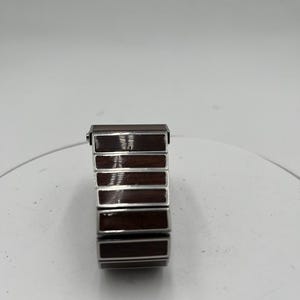 May include: A rectangular watch strap featuring a silver-coloured frame and dark brown wooden inserts. The strap is made up of several rectangular segments, each with a polished wood grain appearance. The watch strap is designed to be flexible and comfortable.