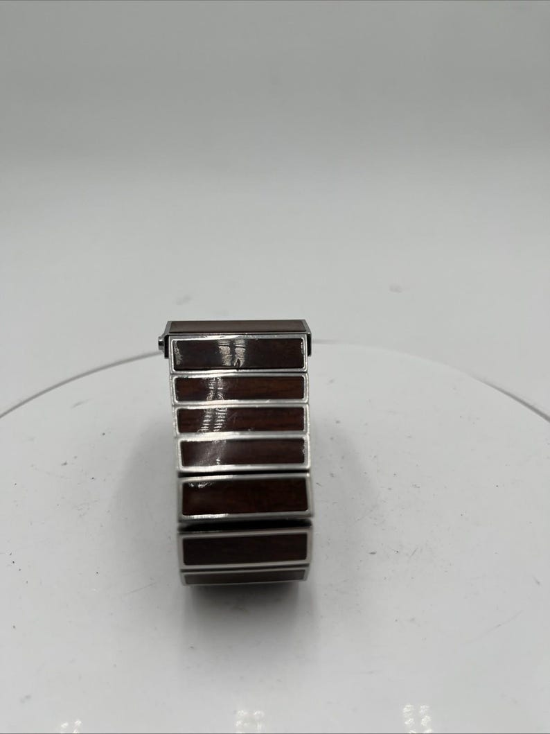 May include: A rectangular watch strap featuring a silver-coloured frame and dark brown wooden inserts. The strap is made up of several rectangular segments, each with a polished wood grain appearance. The watch strap is designed to be flexible and comfortable.