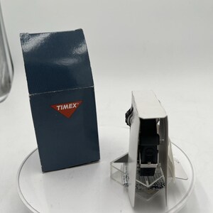 May include: A black Timex watch with a black band is displayed on a white surface. The watch is presented in its original packaging, alongside a navy blue box with the Timex logo.