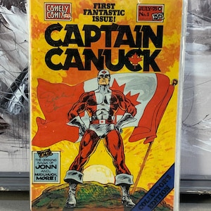 May include: A comic book featuring "Captain Canuck", a superhero, with a Canadian flag on the cover. The cover is predominantly yellow and orange, with text including "First Fantastic Issue!" and "Collector's Edition." The comic is in a protective sleeve.